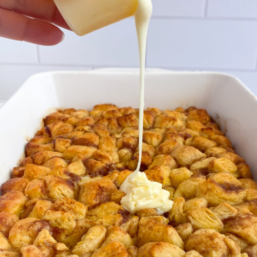 hand pouring frosting over cinnamon roll bake