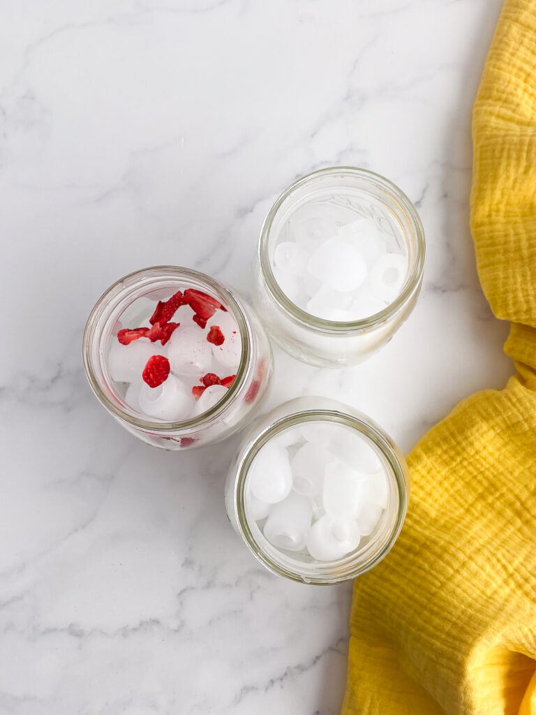 three glass jars on countertop with ice and one with ice and strawberries