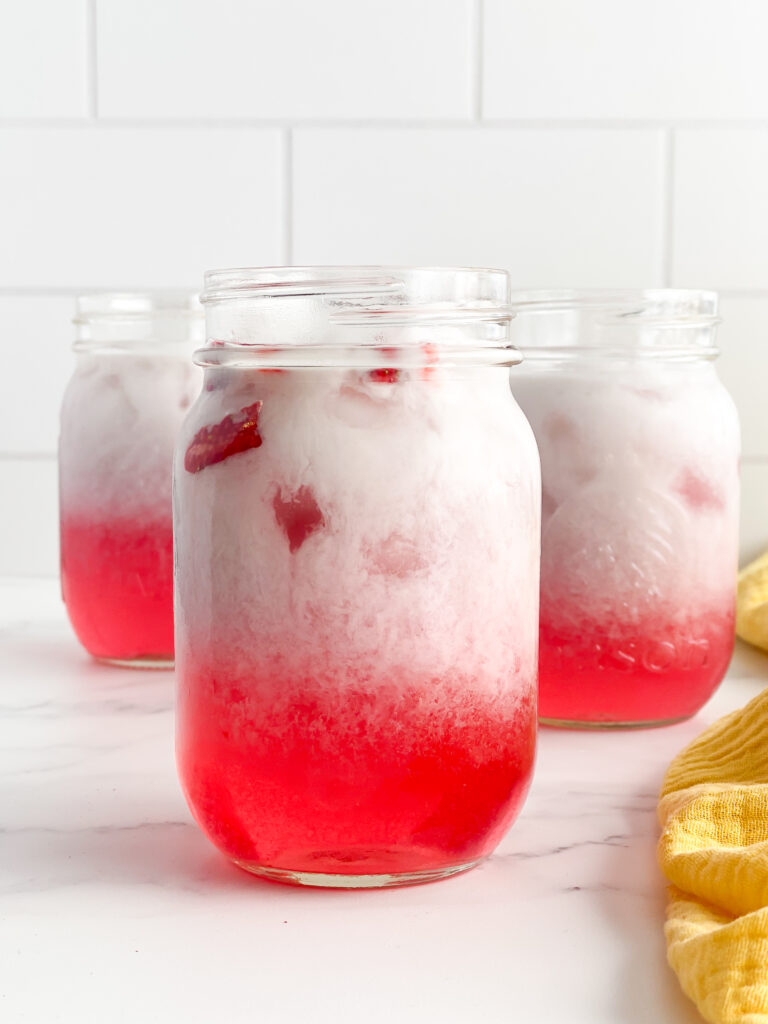 three cups with pink drink and coconut milk in each one on white countertop