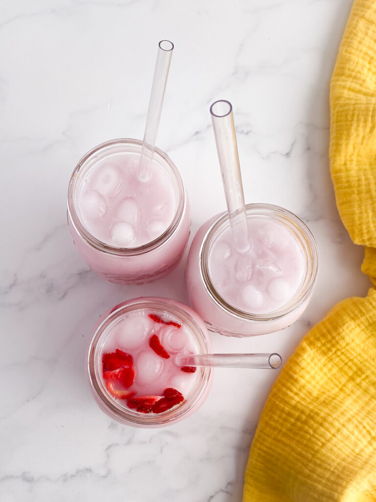 three glass jars on countertop with and pink drink and straws