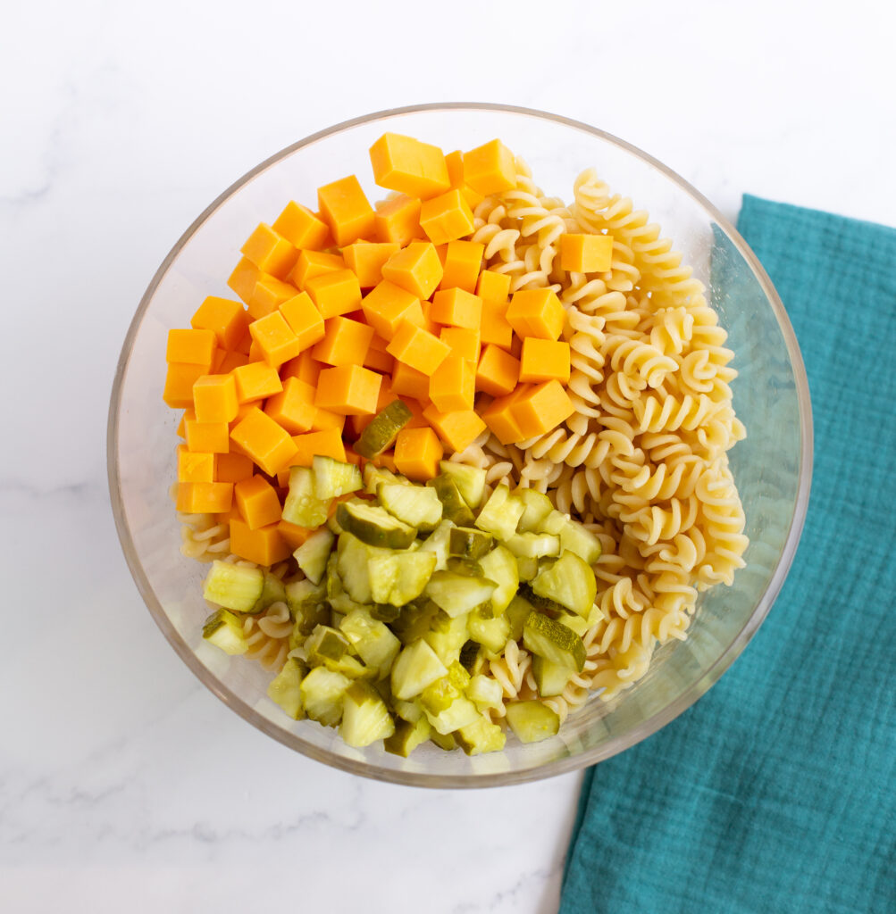 pasta, cheese, and chopped dill pickle in a bowl on a counter top