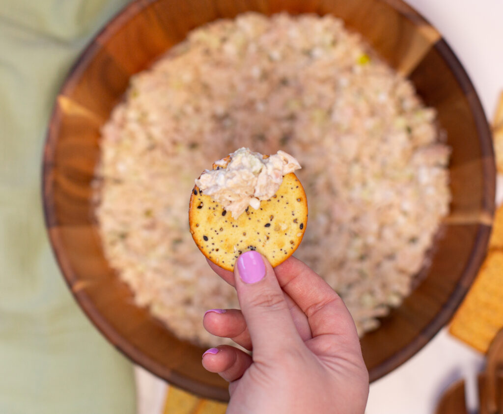 bowl with tuna salad and hand hovering over bowl holding a cracker with tuna salad on the cracker