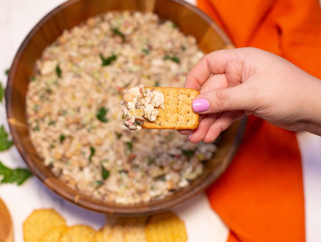 woman holding a cracker above a bowl of tuna salad