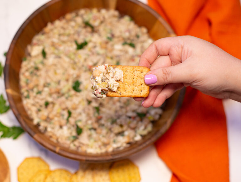 woman's hand holding a cracker with tuna salad hovering above wooden bowl