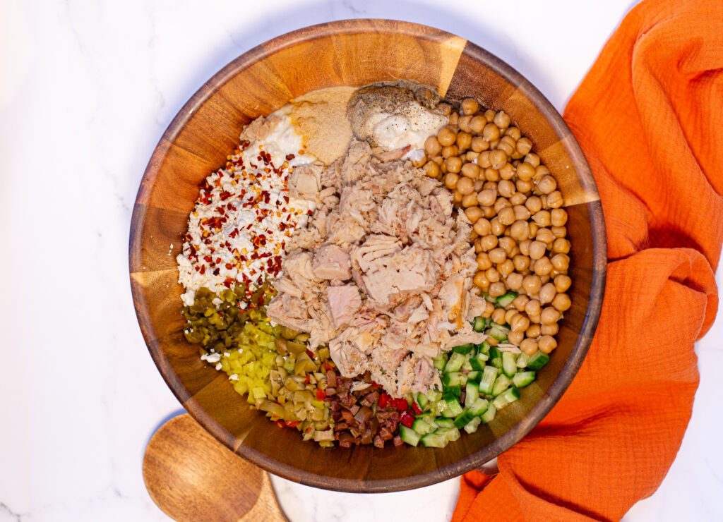 a wooden bowl on a bright white marble surface showing each ingredient that goes into the salad