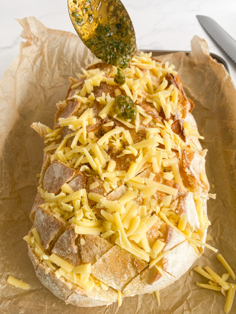 spoon adding butter and herbs to a loaf of bread with shredded cheese all over it