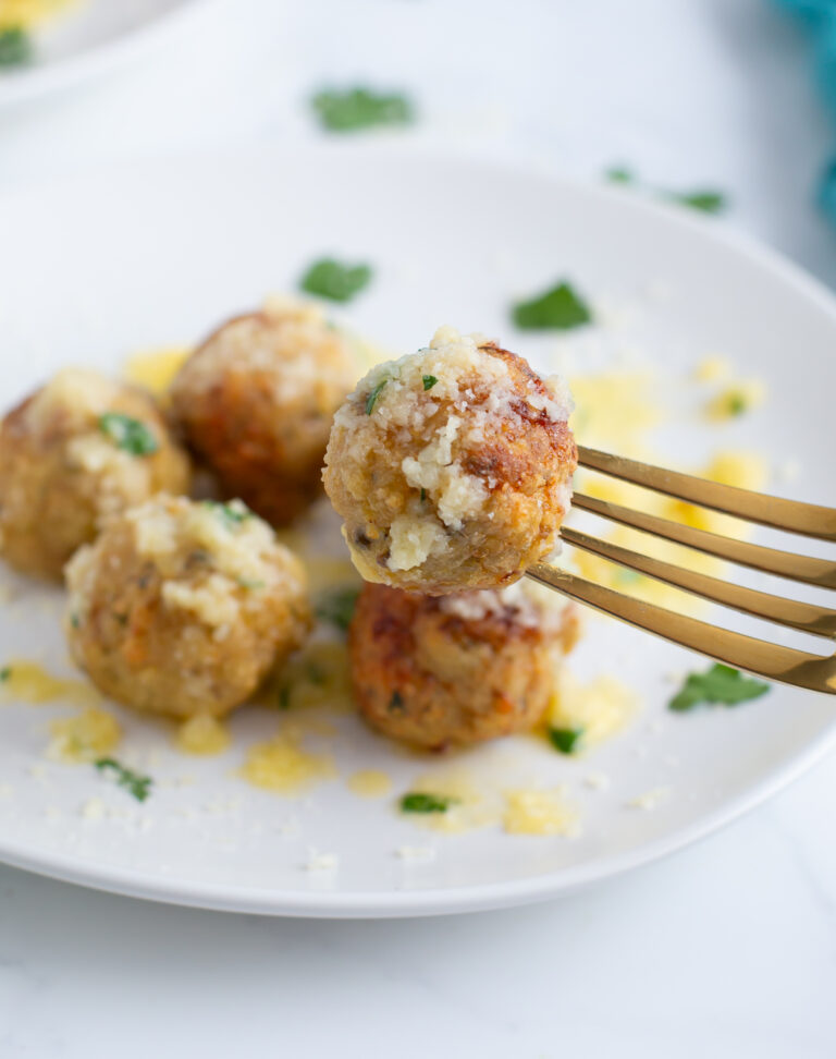 parmesan chicken meatball on a fork above a white plate