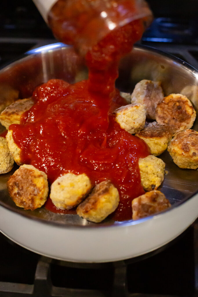 frozen meatballs with marinara sauce being poured over in a pan