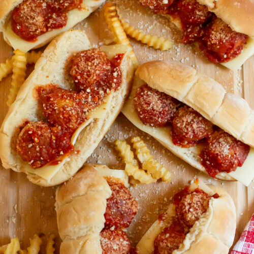 meatball subs and crinkle cut french fries spread out on a cutting board
