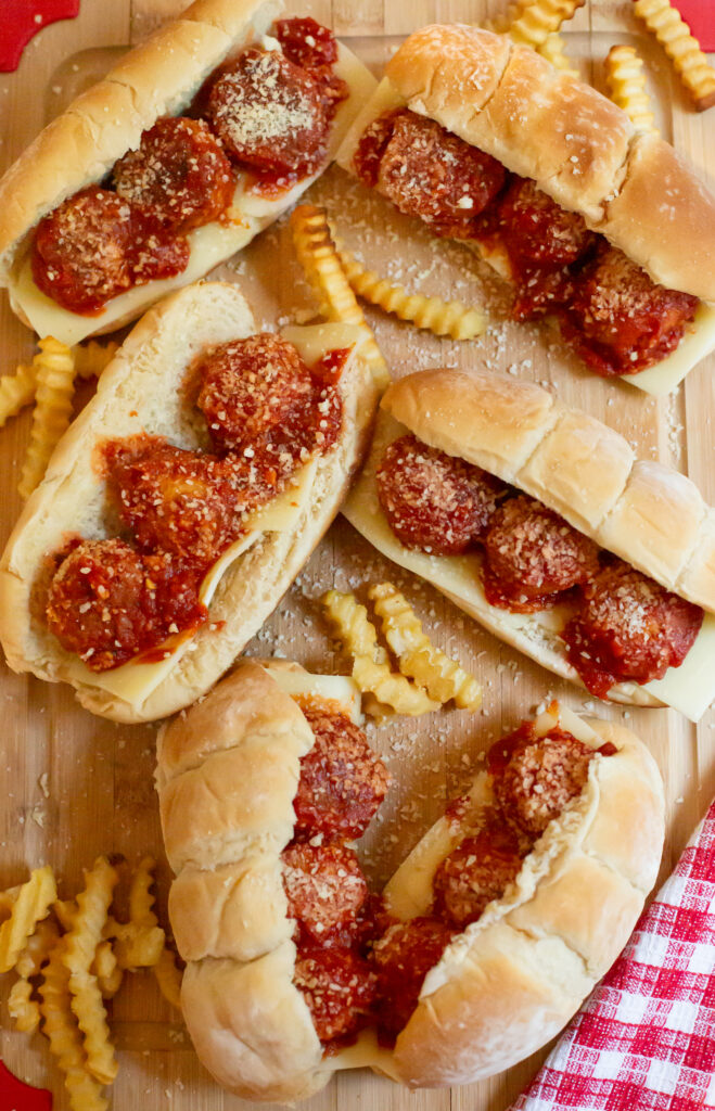 meatball subs and crinkle cut french fries spread out on a cutting board