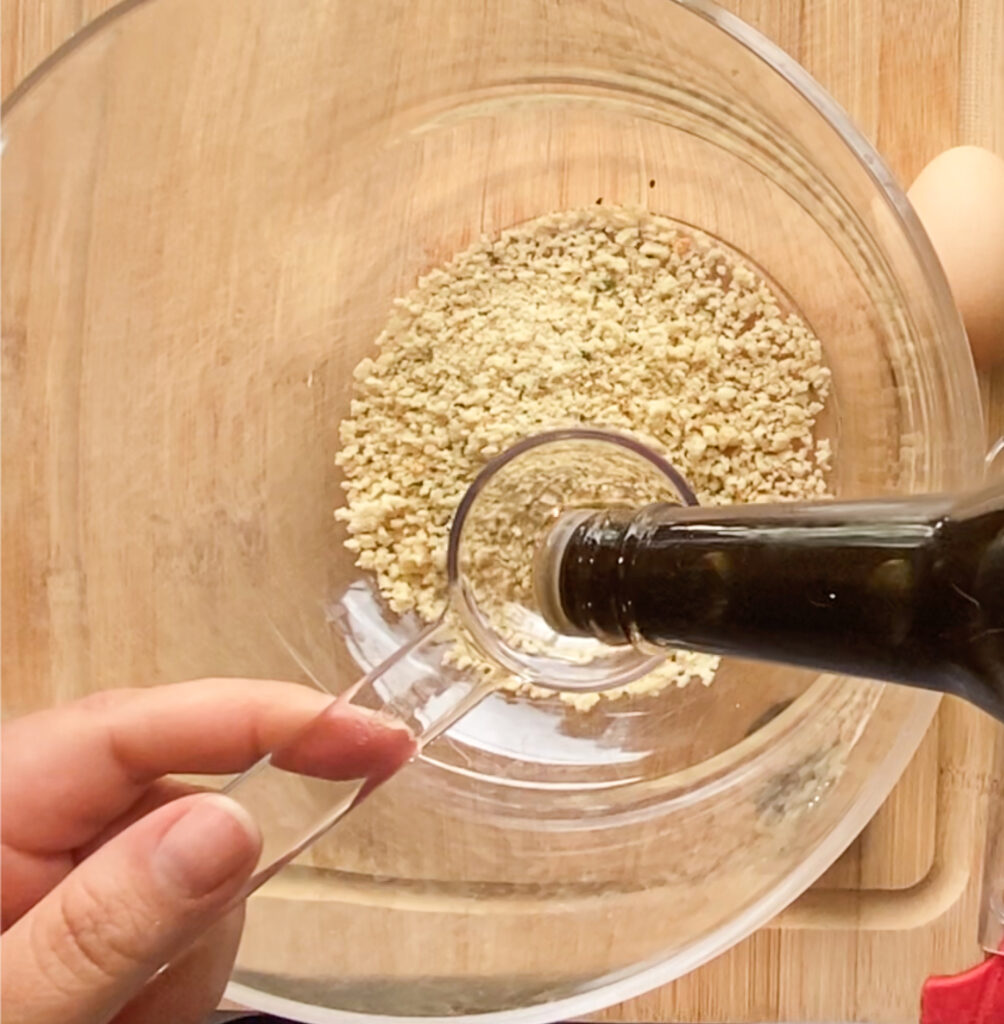 bread crumbs in a bowl with worcestershire sauce being measured into it on a cutting board