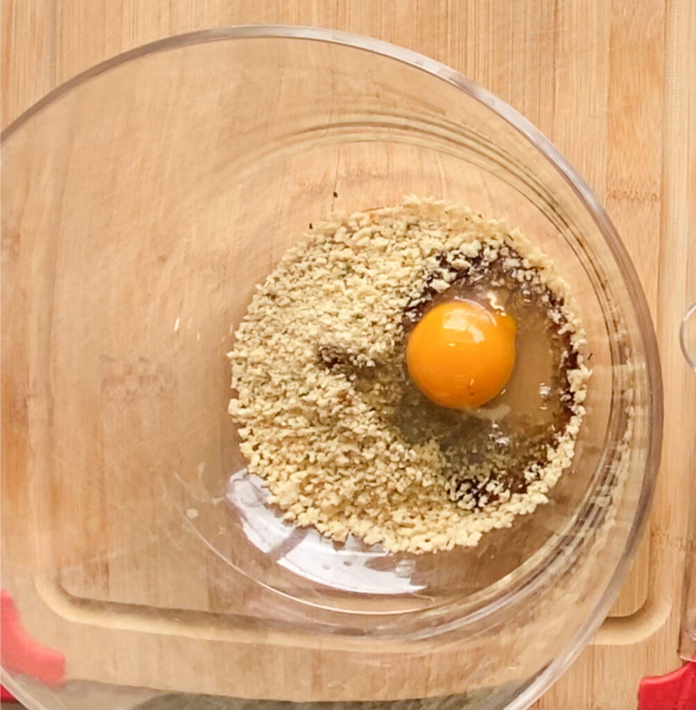 bread crumbs in a bowl with an egg on a cutting board