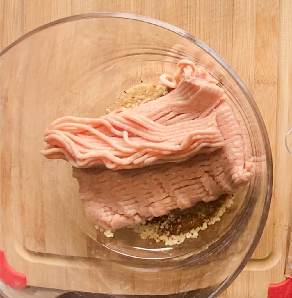 ground chicken in a bowl on top of bread crumbs on a cutting board