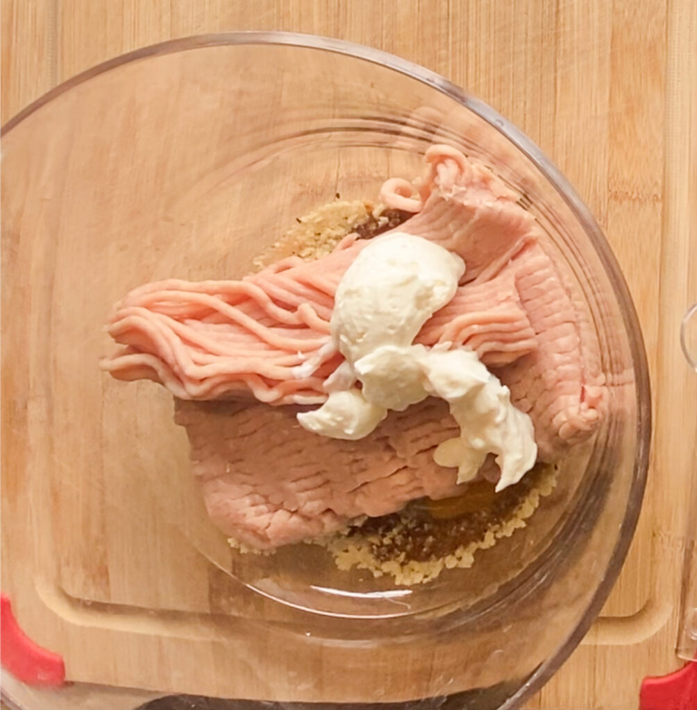 ground chicken in a bowl with mayo measured on top of the chicken on a cutting board