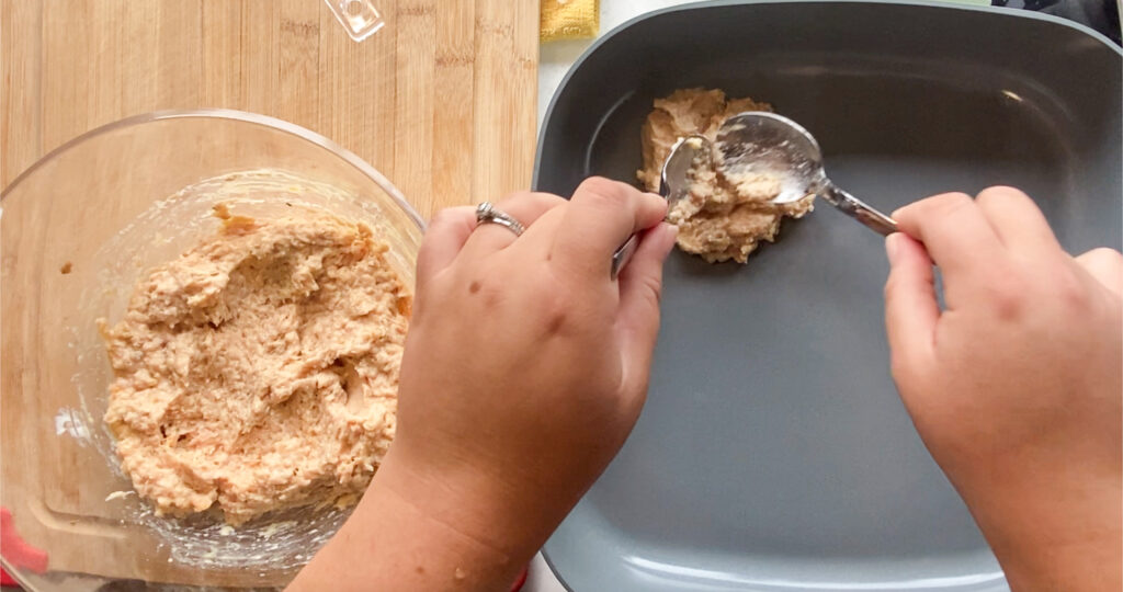 woman's hand spooning over ground chicken burger mixture into a skillet