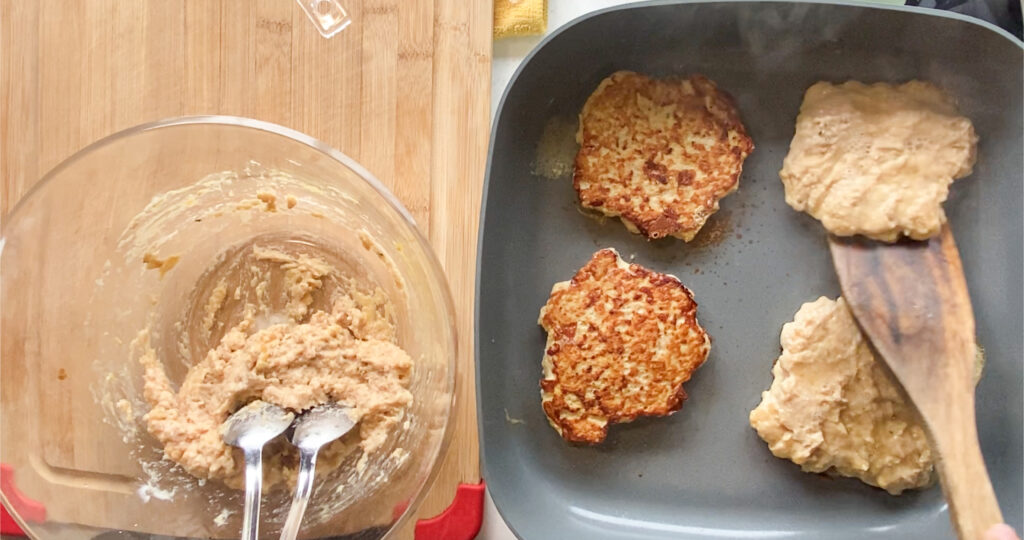 wooden spatula flipping the chicken burgers in a skillet