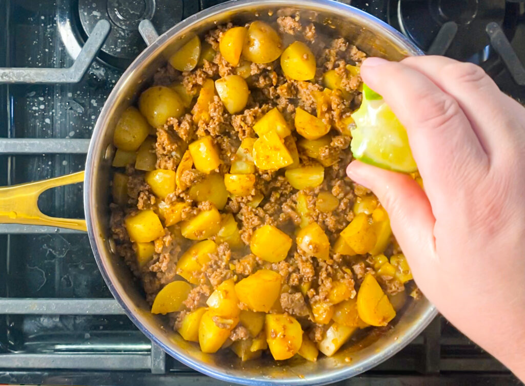 woman's hand squeezing a lime over the ground beef and potatoes in a pan