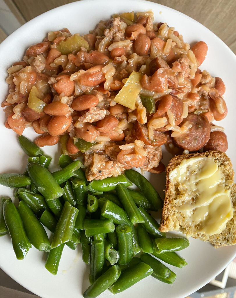 a white plate with rice and pinto beans, green beans, and buttered bread