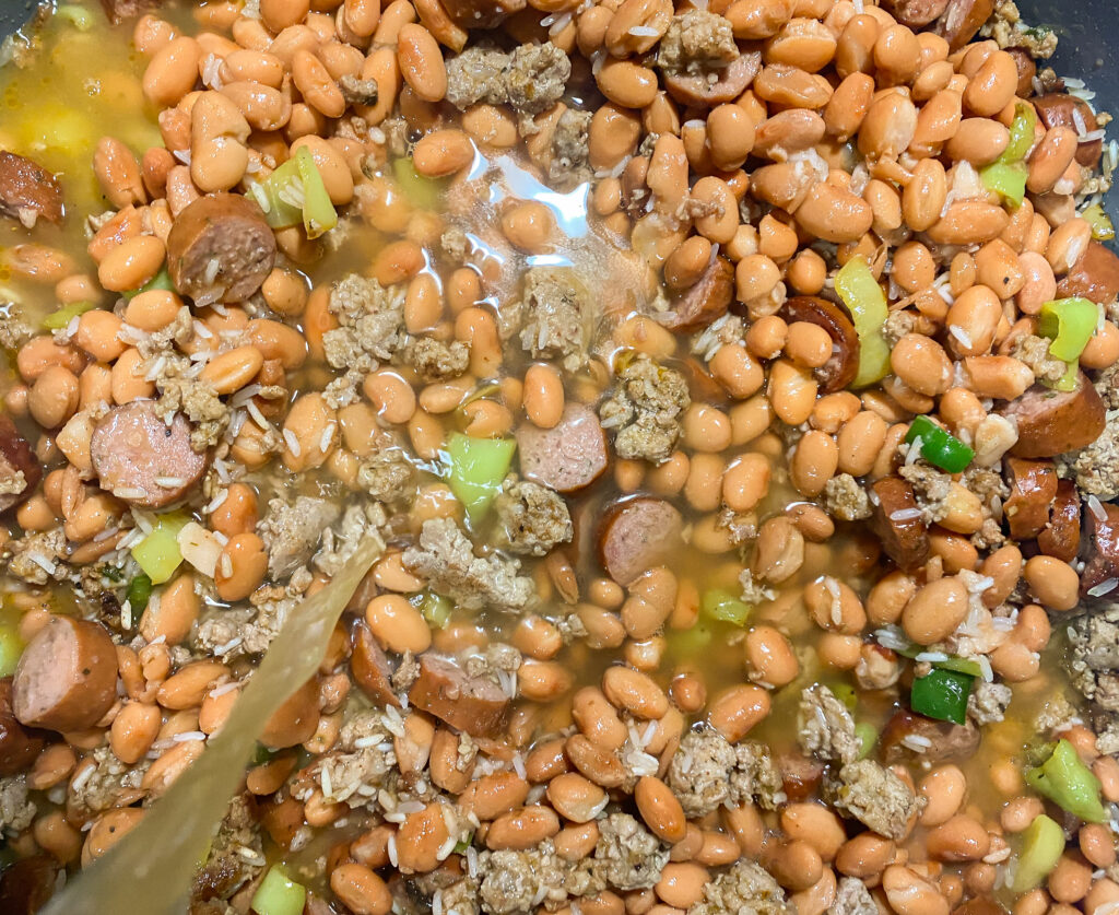 broth being poured into skillet of beans and meat