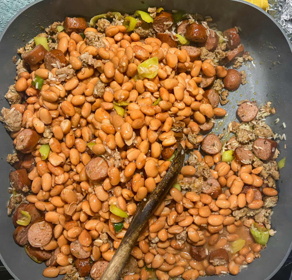 pinto beans on top of meat, rice, and peppers in a skillet