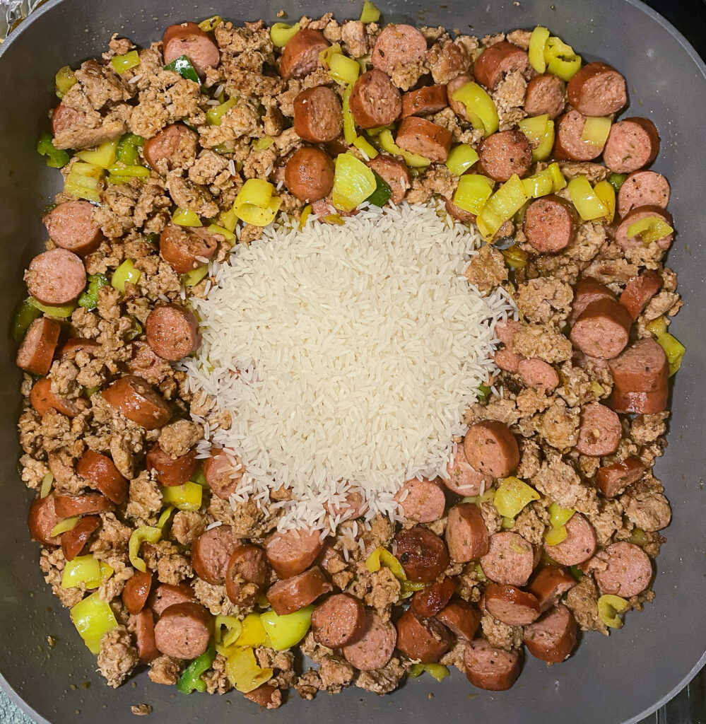 white rice topped the sausage, ground meat, and pepper mixture in a skillet