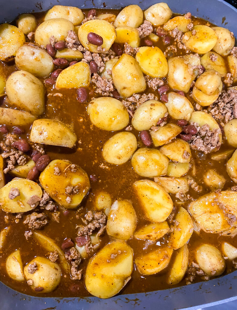 the ingredients of potatoes, chili beans, ground meat, chili seasonings all mixed together in a skillet