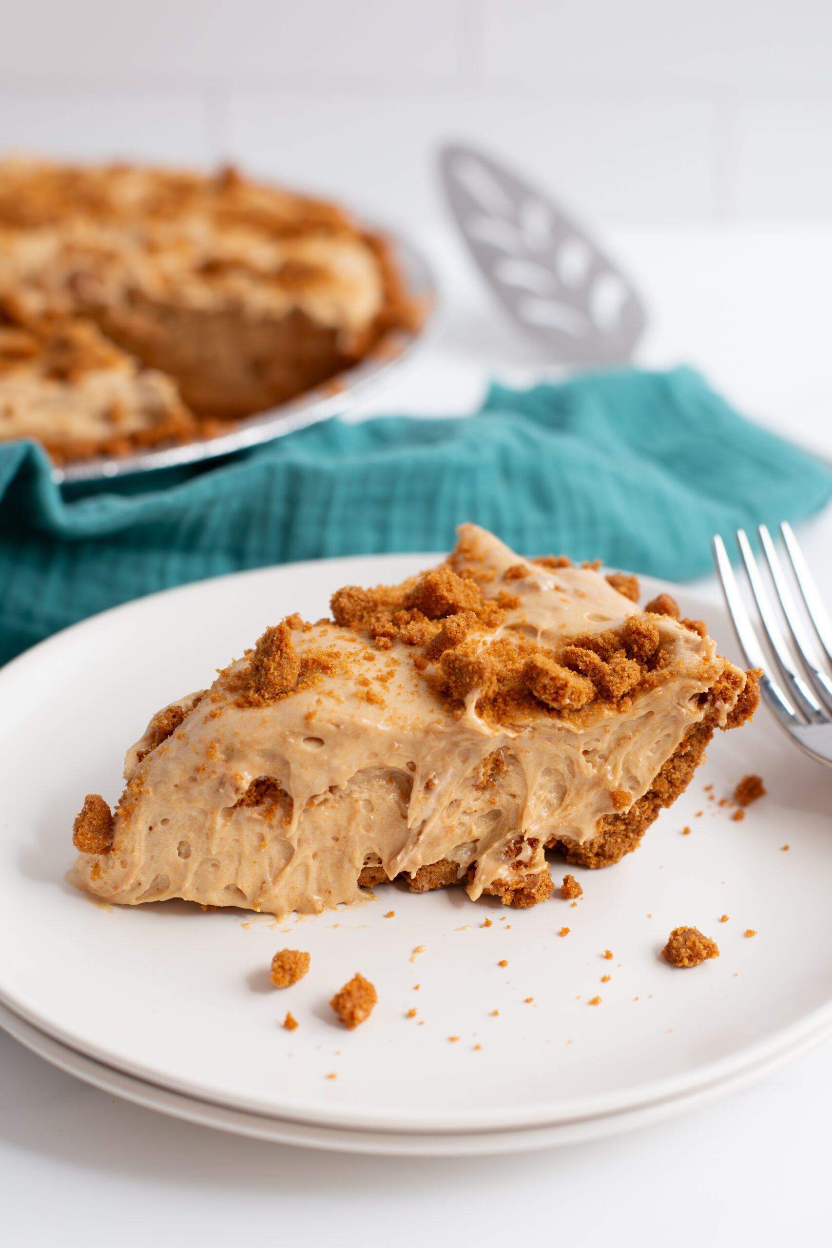 a Biscoff cookie pie slice from the pie pan on a white countertop with a blue hand towel