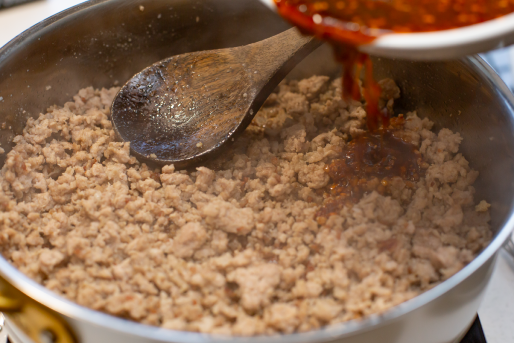 cooked ground pork with sauce being poured into the pan
