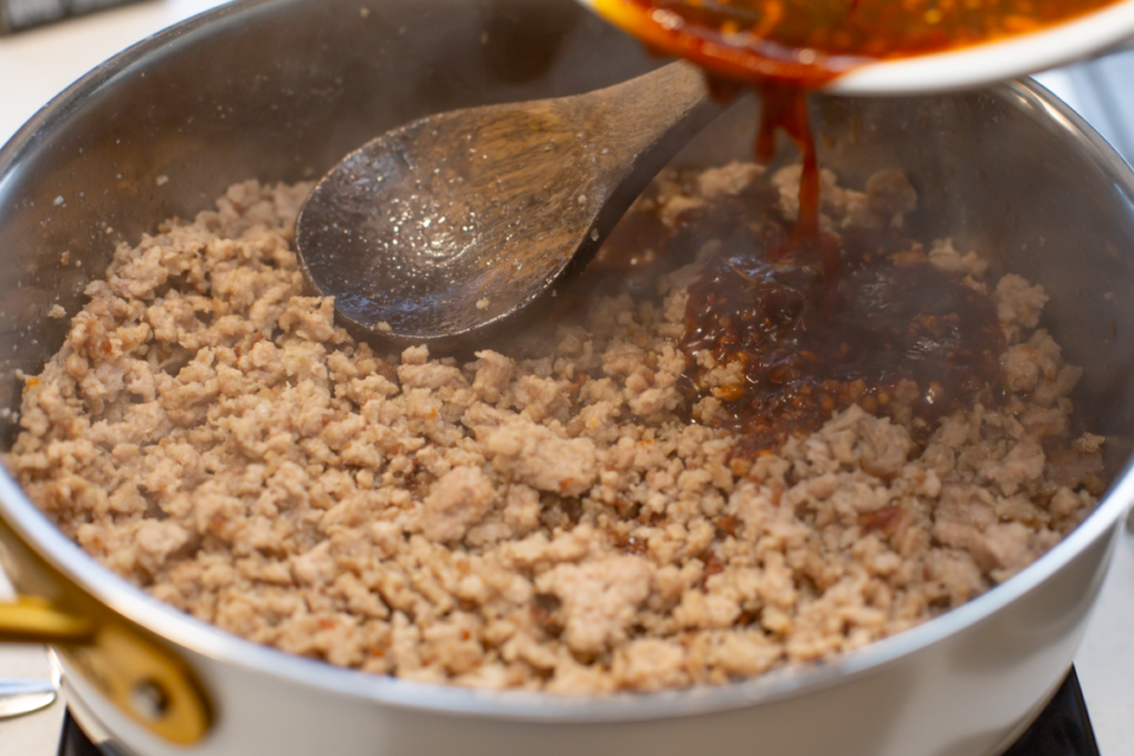 cooked ground pork with sauce being poured into the pan