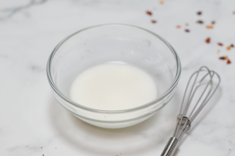 cornstarch slurry in a clear bowl on a white counter with a whisk next to it