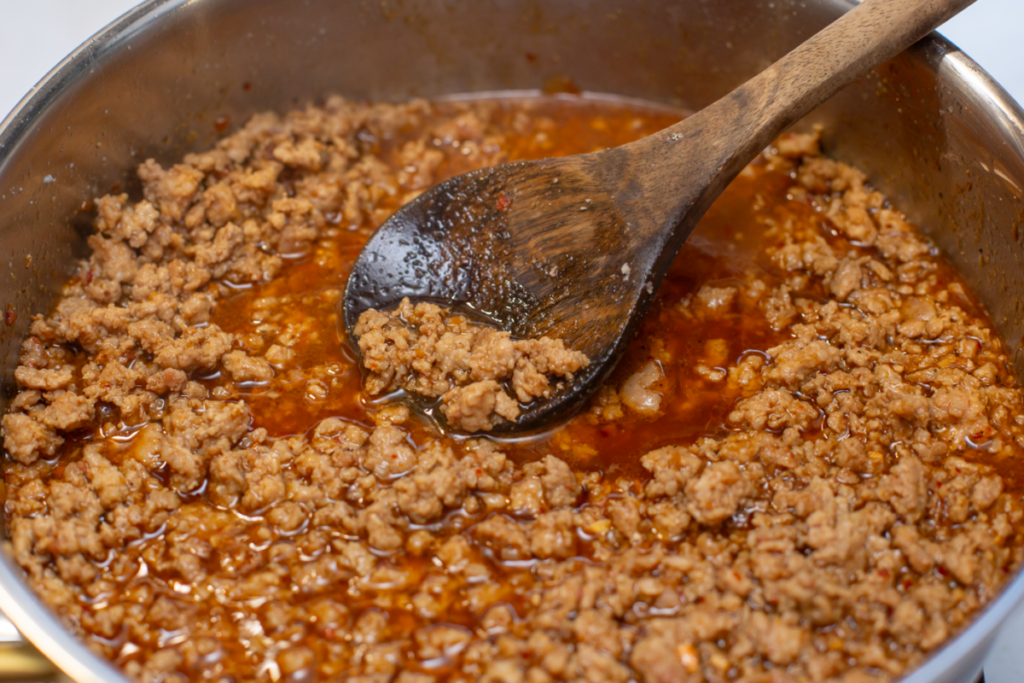 asian pork and sauce being stirred by a wooden spoon in a pan