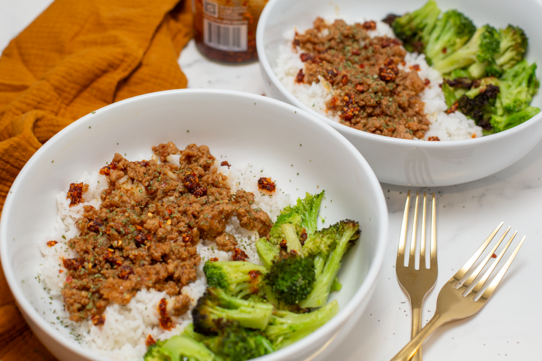 easy asian ground pork and rice in a white bowl with broccoli and gold forks on the white counter next to the bowl