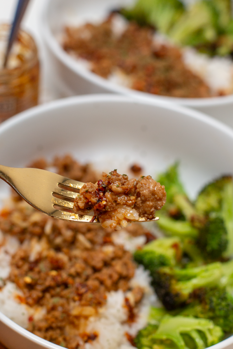 asian pork and rice on a fork above a white bowl