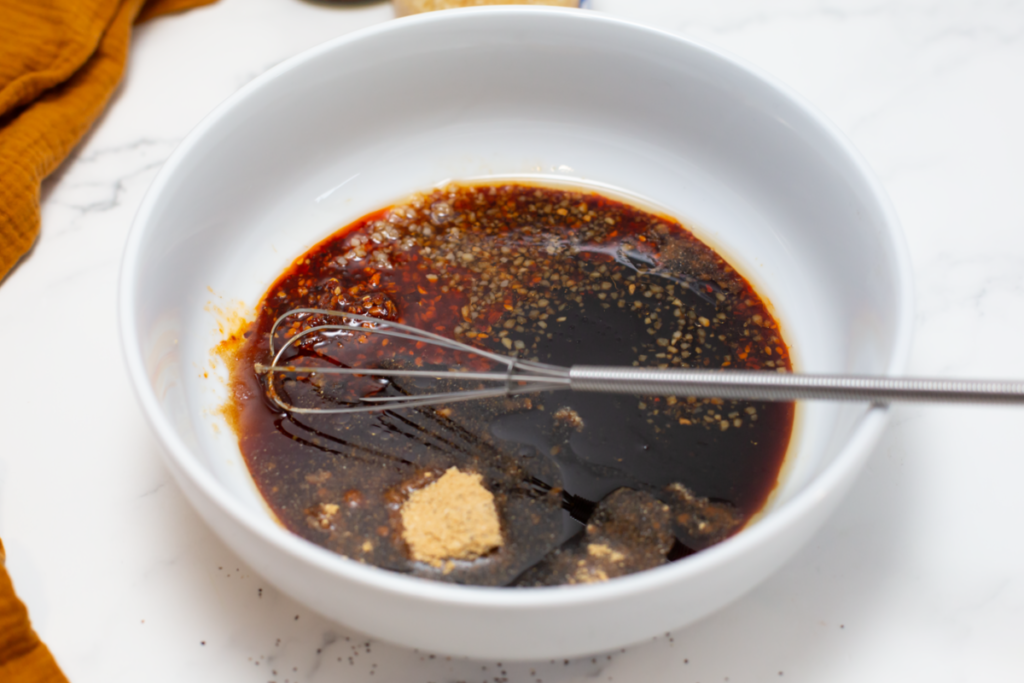 sauce in a white bowl on a white counter with a whisk in the bowl