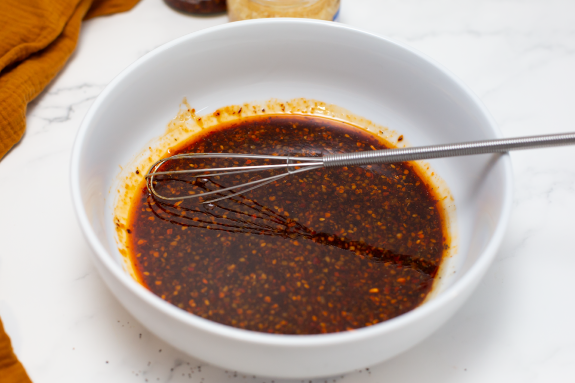 stirred sauce in a white bowl on a white counter with a whisk in the bowl