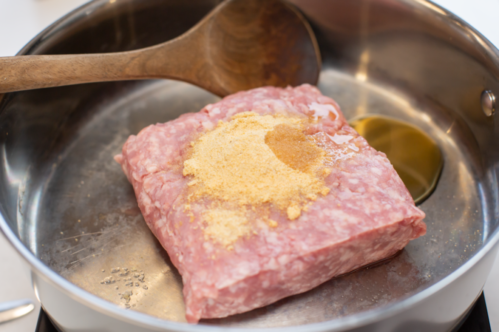 uncooked ground pork with sesame oil and seasonings in a pan