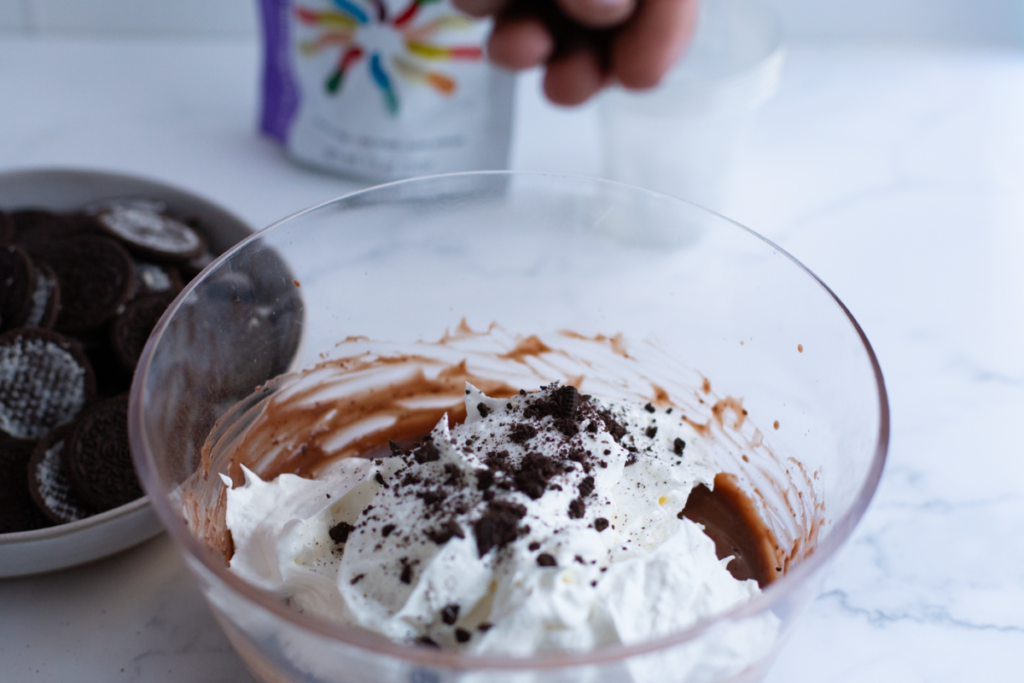 pudding and cool whip with oreo cookies being put in the bowl
