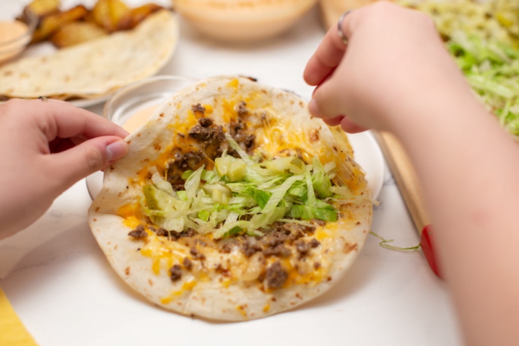 lettuce and pickles being added to the inside of the quesadilla burger