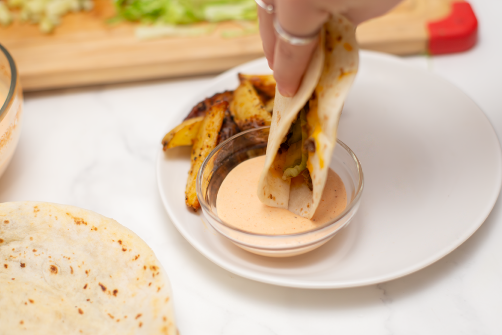 hand dipping the quesadilla in the burger sauce on a white plate