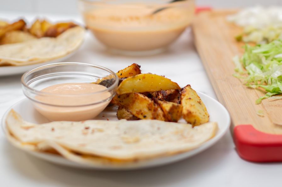 quesadilla burger on a white platte with a bowl of burger sauce and a side of potatoes