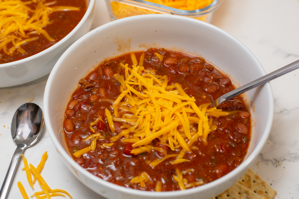 bowl of chili with cheese on top and spoon in bowl on a white counter