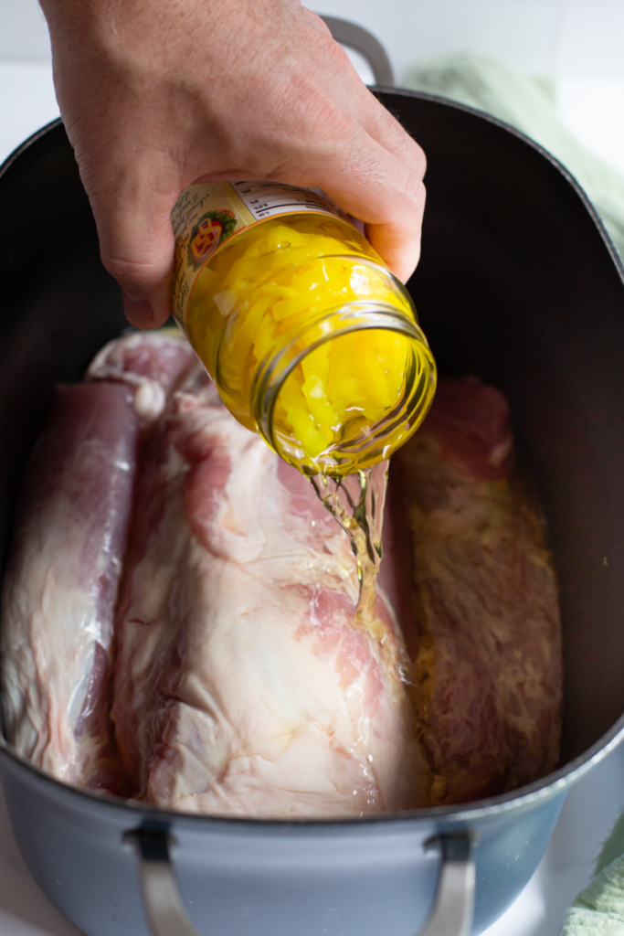 banana pepper brine being poured onto raw pork loin in a slow cooker