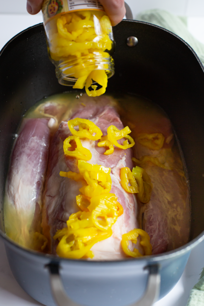 banana pepper jar being poured onto raw pork loin in a slow cooker