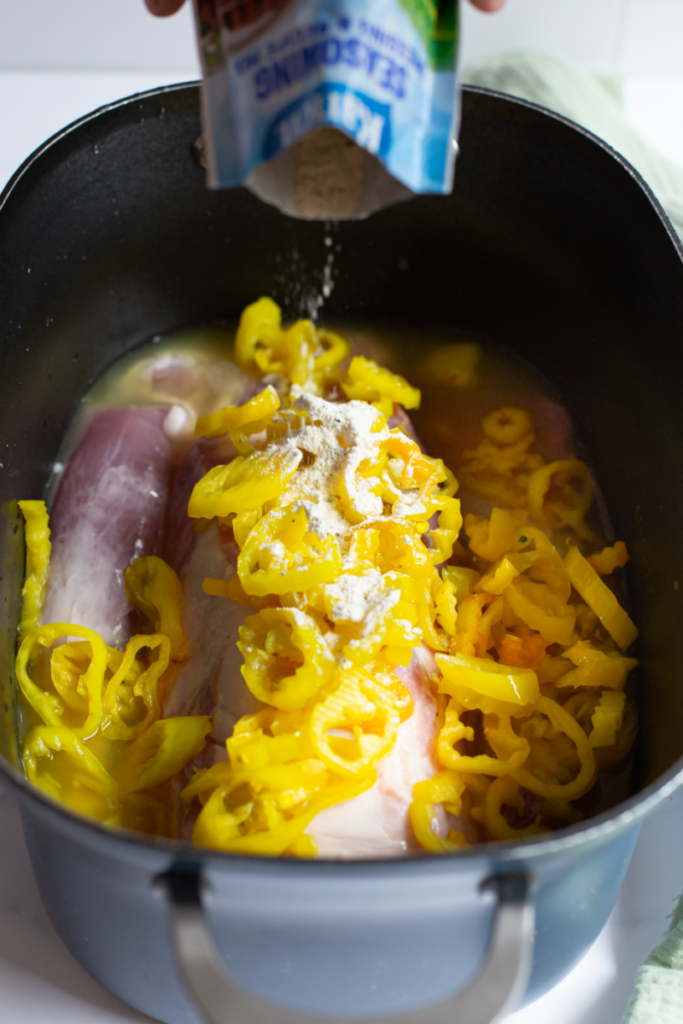 ranch packet seasoning being poured onto raw pork loin in a slow cooker