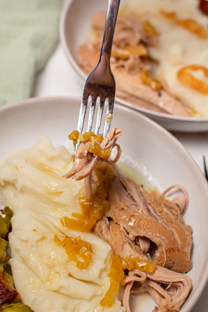 mississippi pork loin on a fork above a plate of mashed potatoes