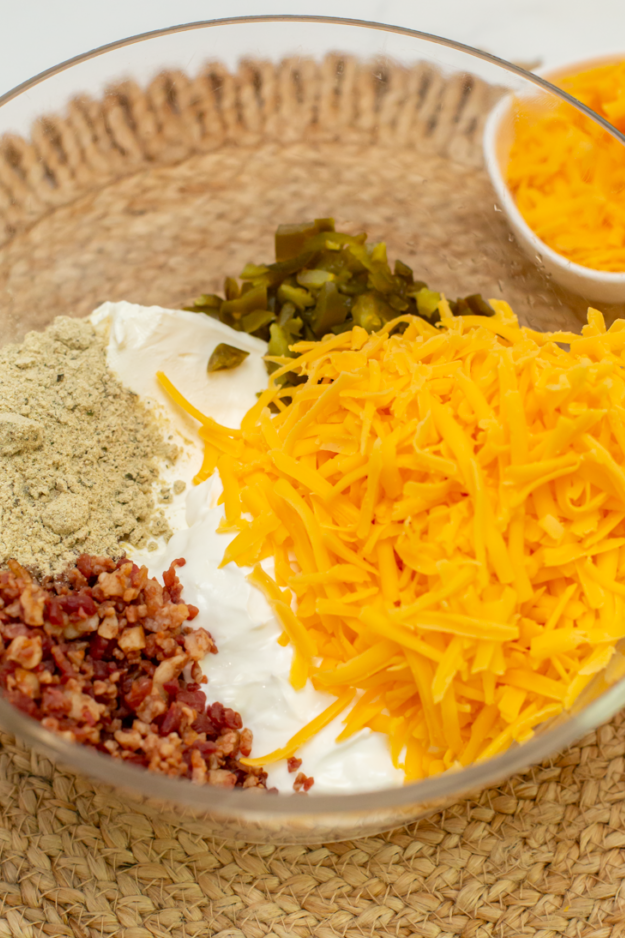 all of the ingredients for creamy cheddar jalapeno bacon ranch dip in a mixing bowl on a brown surface