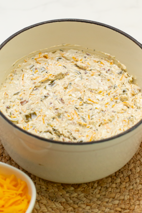 all of the ingredients for creamy cheddar jalapeno bacon ranch dip mixed together in a serving crock on a brown surface