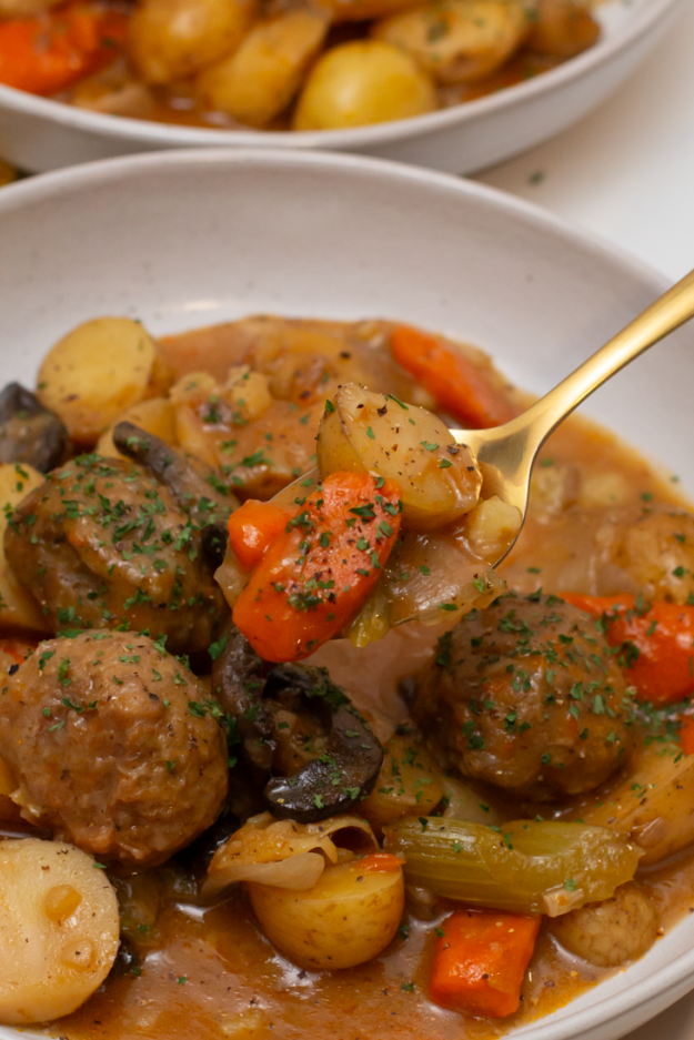 A spoonful of meatball stew showing a carrot and potato. 