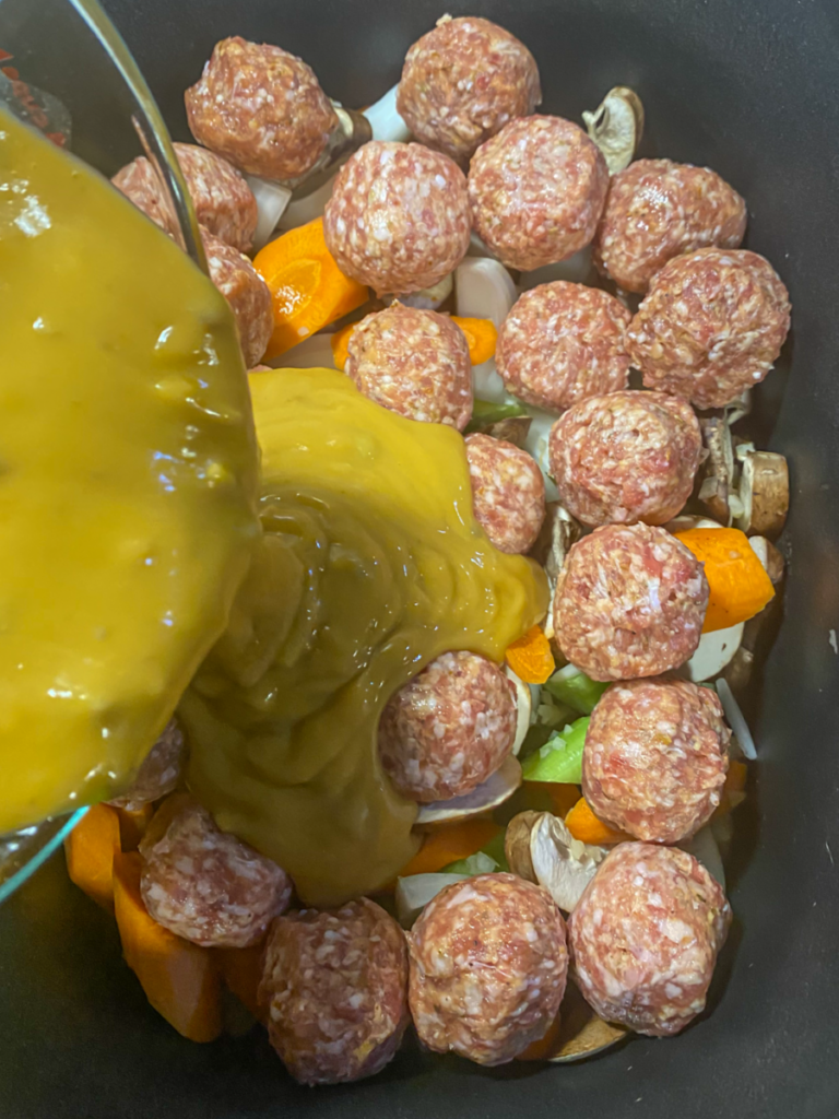 The sauce being poured into the slow cooker over the meatballs and vegetables.
